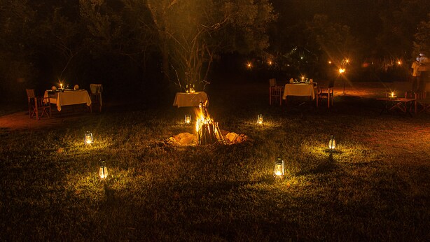 An outdoor dining area with tables and chairs arranged around a central fire pit, illuminated by lanterns. - Big Game Yala by Eco Team (Kataragama)