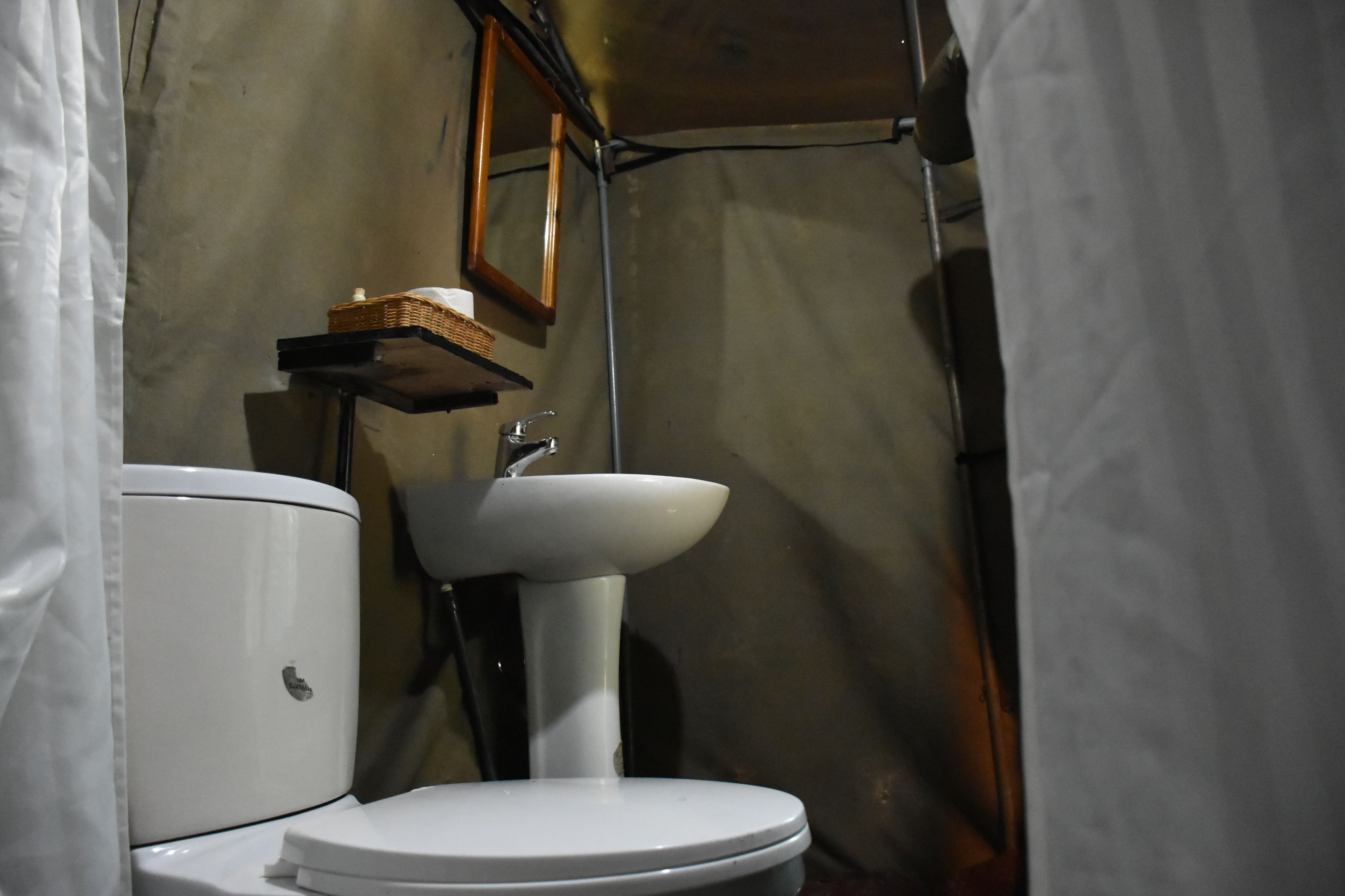 A compact bathroom with a white toilet, a white sink, and a small shelf with a basket.