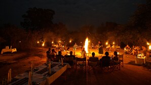An outdoor dining area with tables set for a meal, surrounded by trees and a campfire in the background. - Big Game - Udawalawe by Eco Team (Thanamalvila)