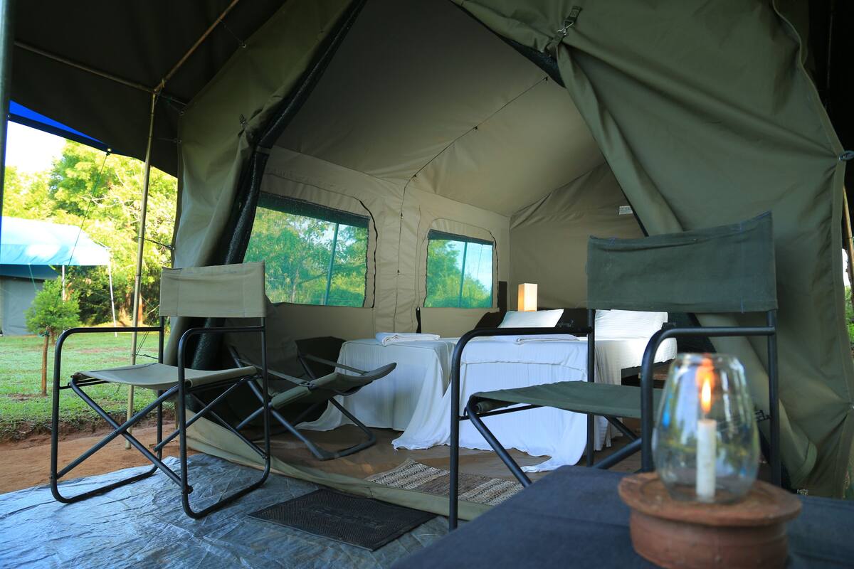 A tented accommodation with two foldable chairs, a small table, and a candle on a wooden base.