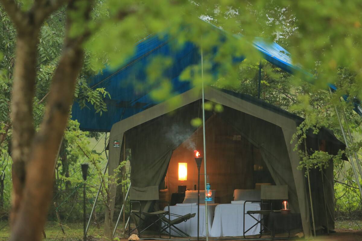 A tent with a table and chairs set up inside, surrounded by trees.