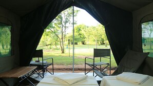 A tent with two beds, a table, and chairs, with a view of a grassy area and trees. - Big Game - Wilpattu by Eco Team (Pahala Maragahawewa)