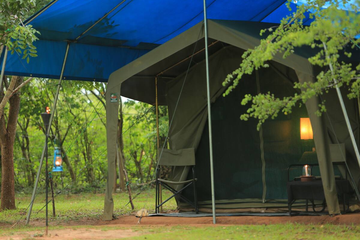 A tent with a blue canopy, a table with a lamp, and a chair.