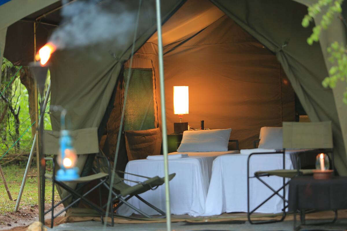 A tent with a bed, two chairs, and a table with a lamp.