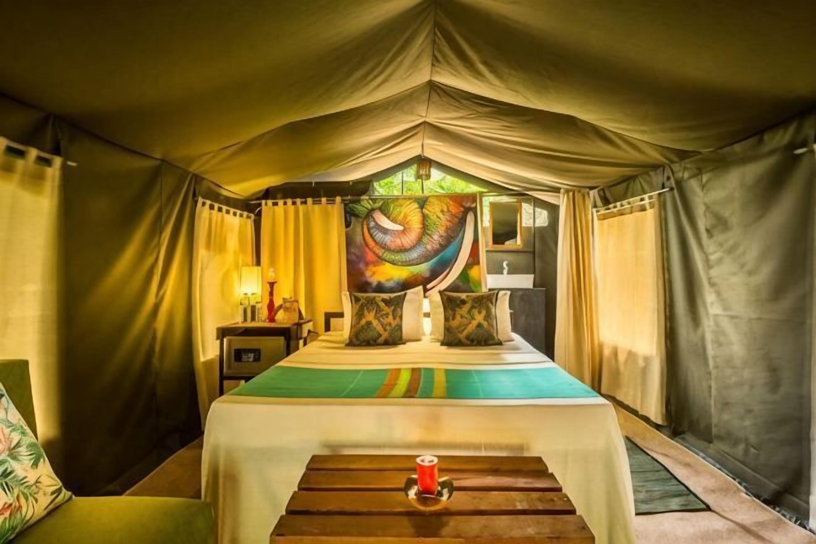 A tented room with a bed, pillows, a nightstand, and a table with a candle.
