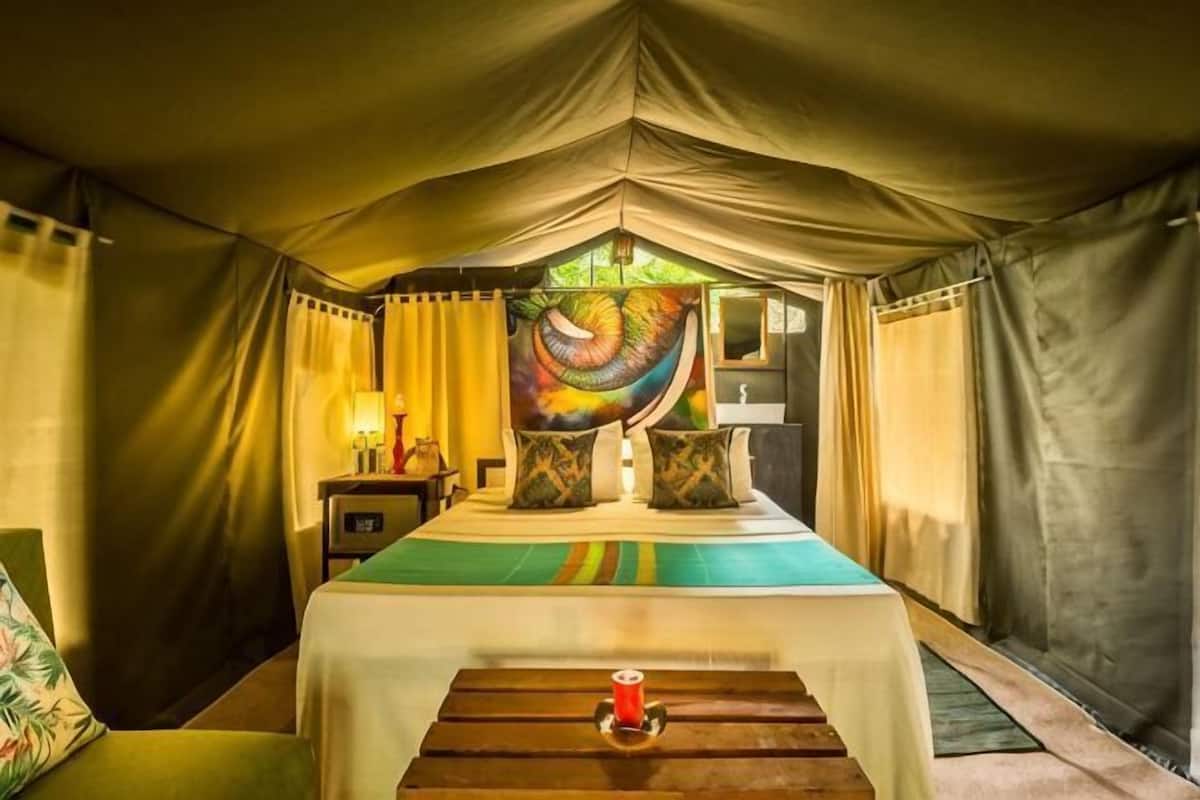 A tented room with a bed, pillows, a nightstand, and a table with a candle.