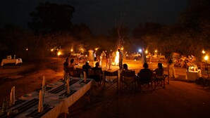 An outdoor dining area with tables set up for a meal, surrounded by trees and a campfire in the center. - Big Game - Wilpattu by Eco Team (Pahala Maragahawewa)
