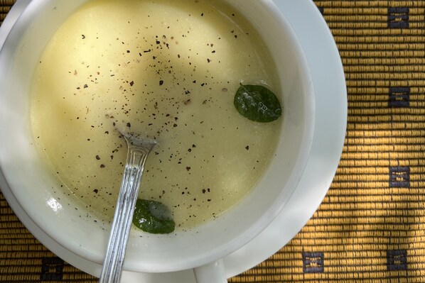A bowl of soup with a clear liquid, a spoon, and a green leaf.