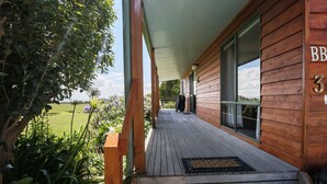 A wooden building with a covered porch, a number '3' sign, and a view of a green landscape. - Buln Buln Cabins (Yanakie)