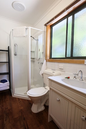 A bathroom with a glass shower enclosure, a white toilet, a sink with a mirror, and a window above the sink.