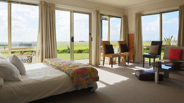 A hotel room with a large bed, two chairs, a small table, and a view of the countryside. - Buln Buln Cabins (Yanakie)