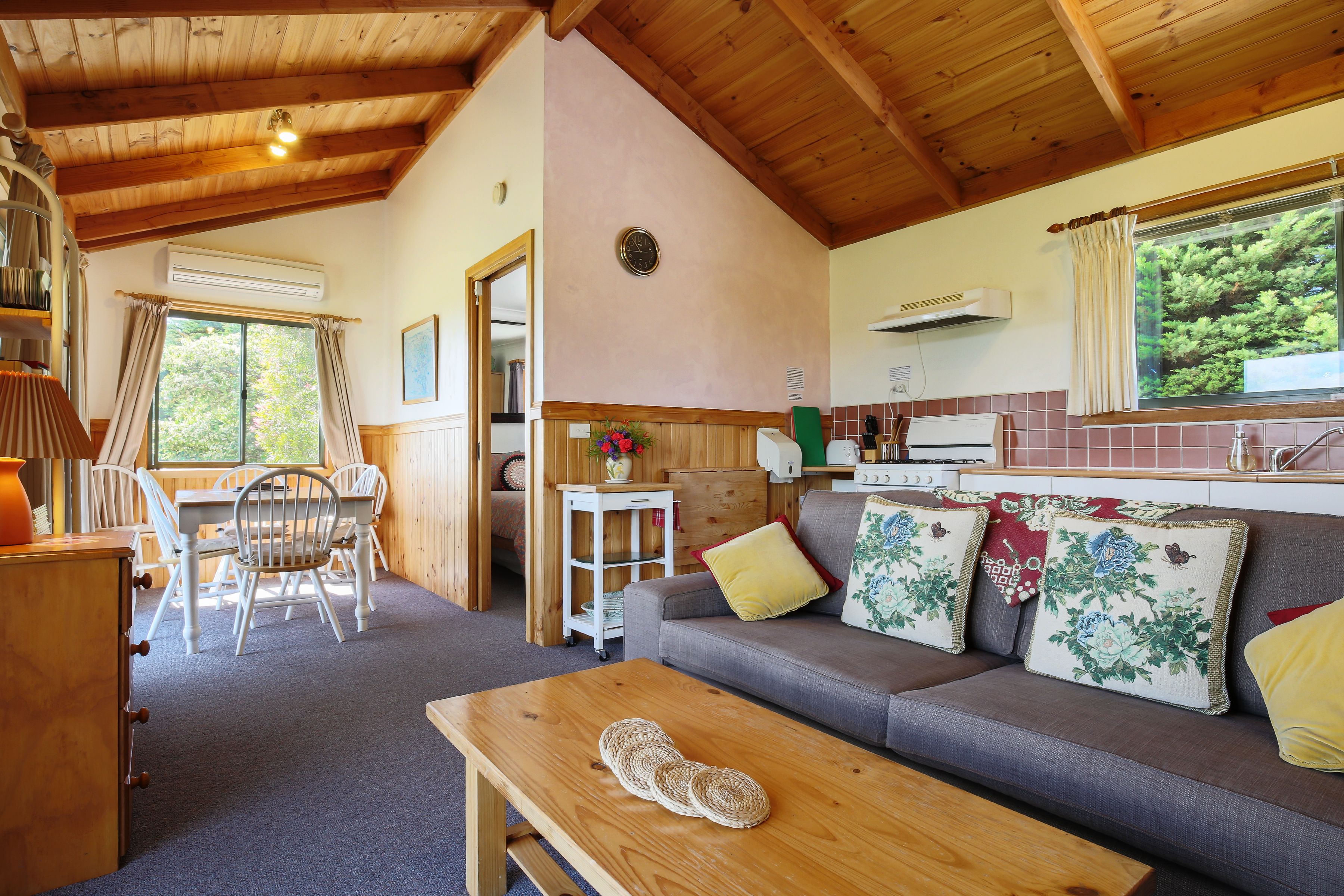 A cozy cabin interior with a dining area, sofa with floral cushions, and a wooden table.