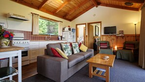 A cozy cabin interior with a wooden ceiling, a kitchenette, a sofa with cushions, a dining table, and a TV. - Buln Buln Cabins (Yanakie)
