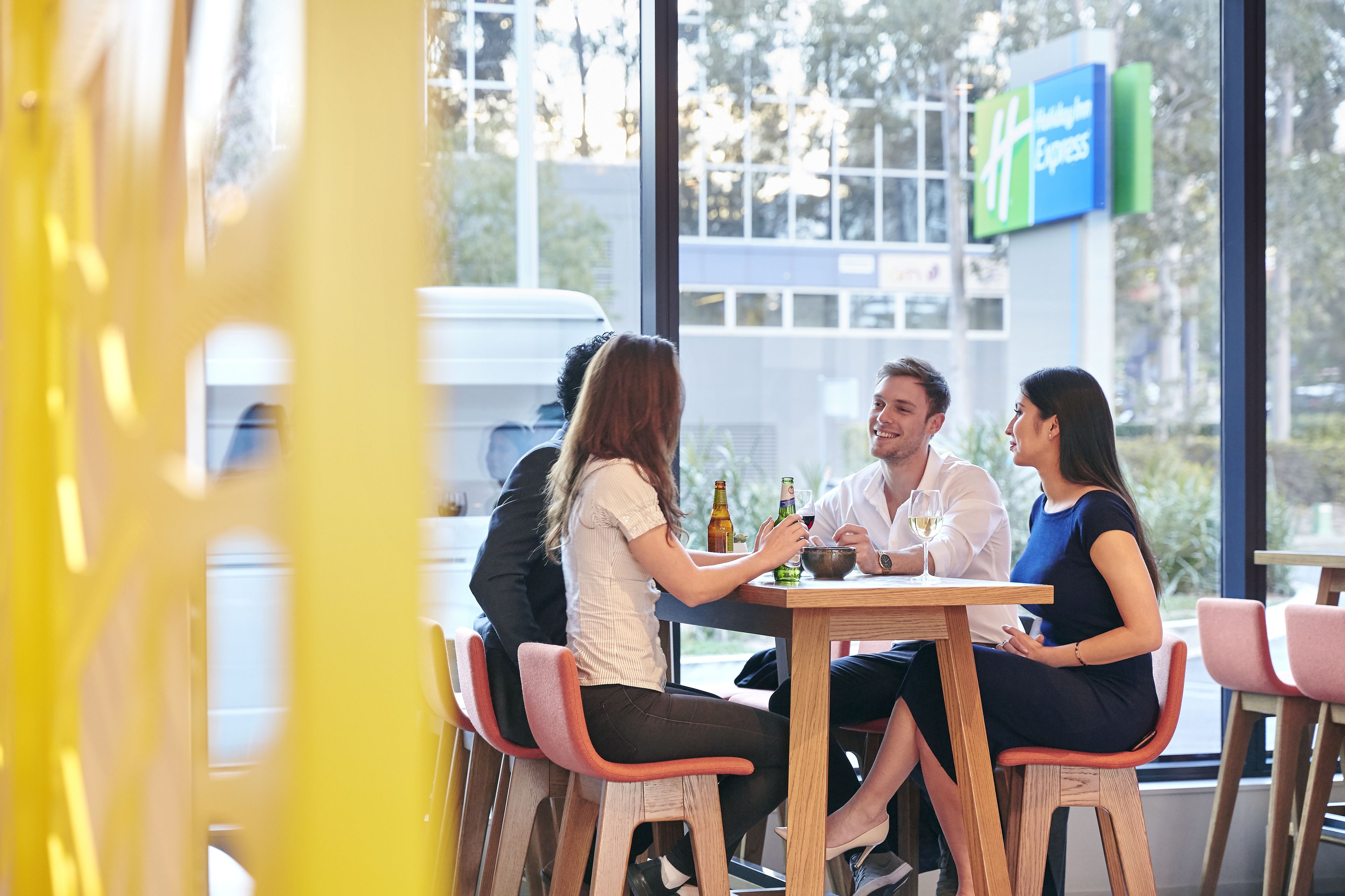 Um grupo de pessoas jantando à mesa com vista para um letreiro de hotel ao fundo.