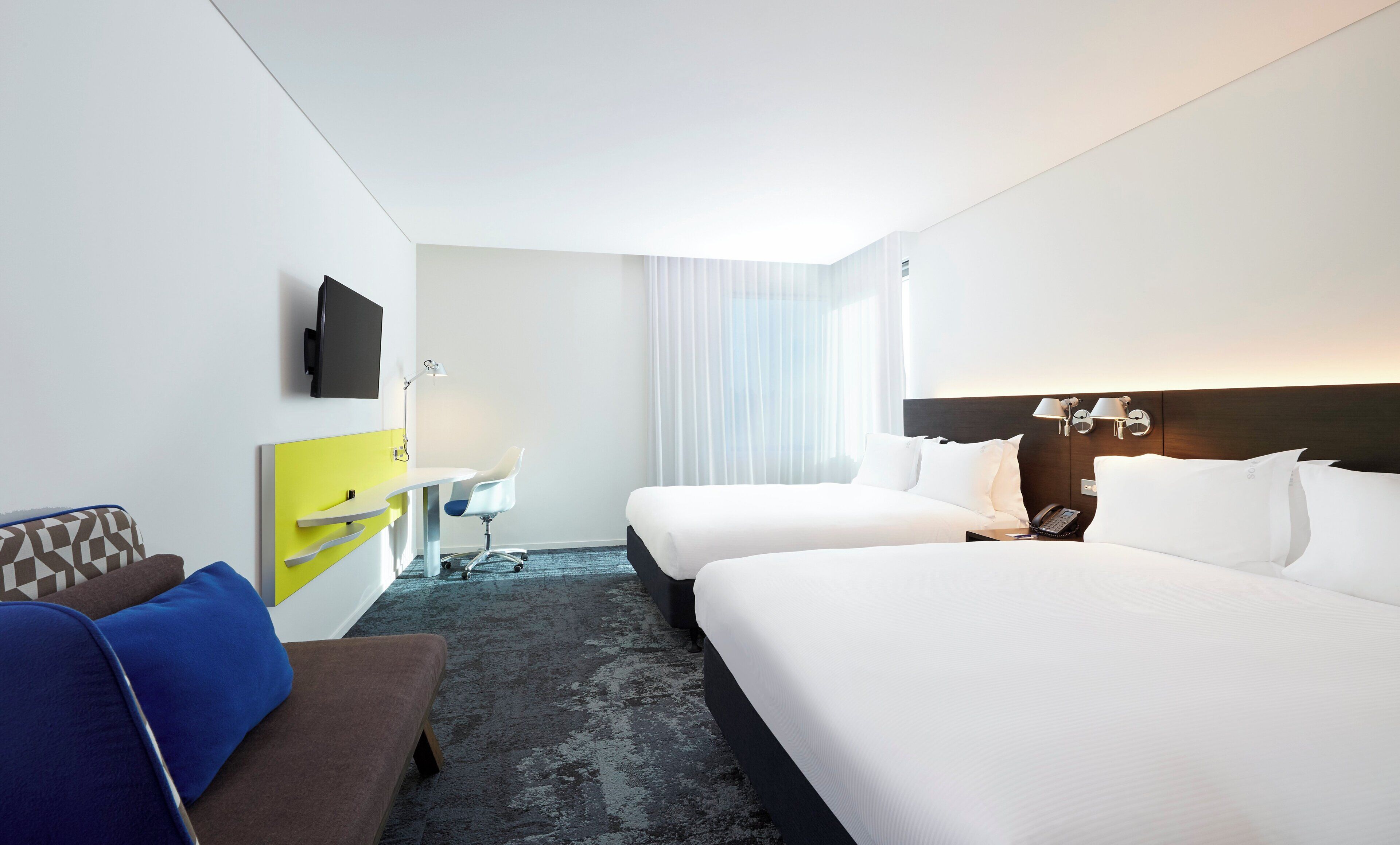 A hotel room with two beds, a desk, a chair, a TV, and a phone.