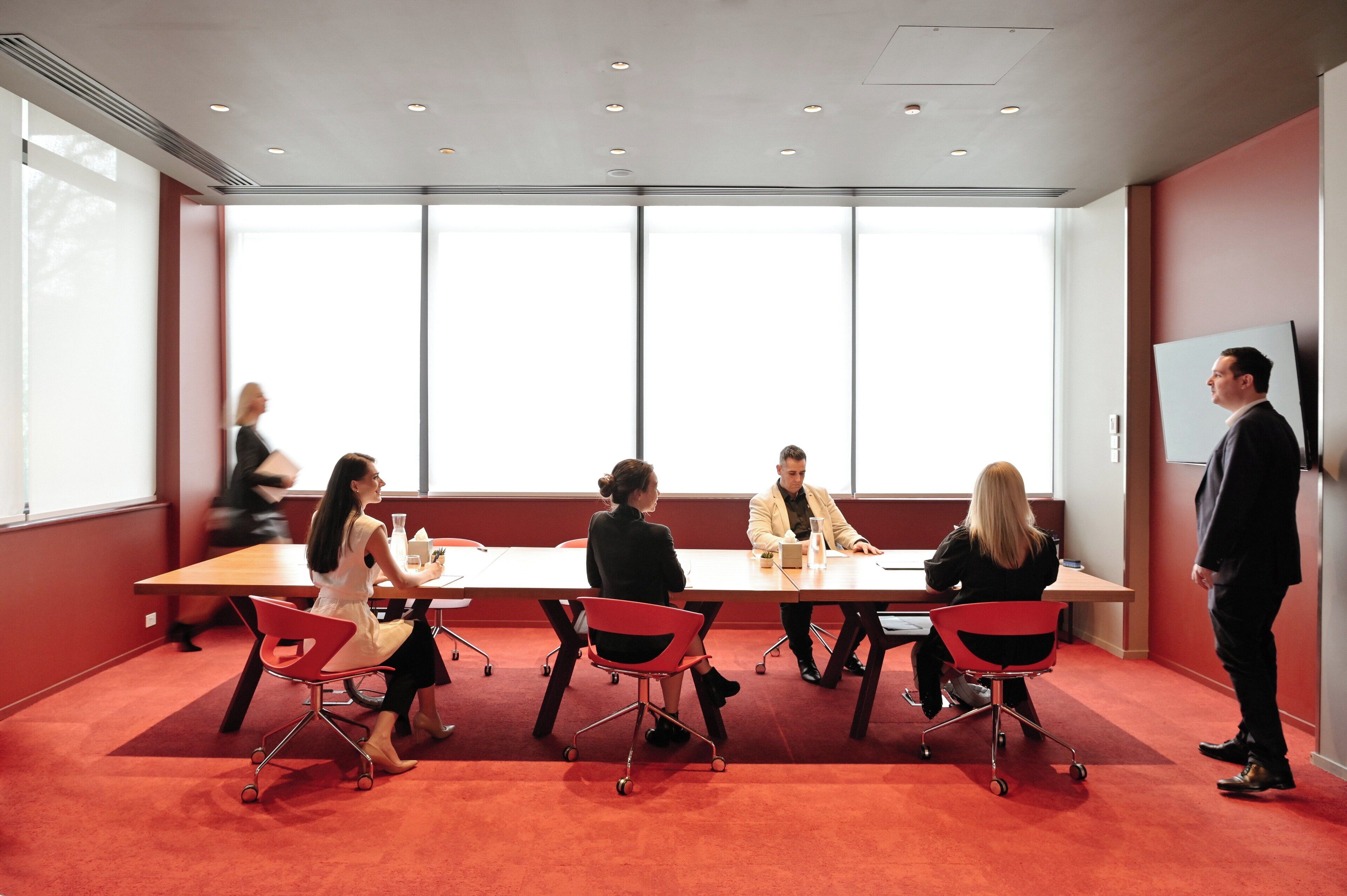 A conference room with a large table, red chairs, and a whiteboard.