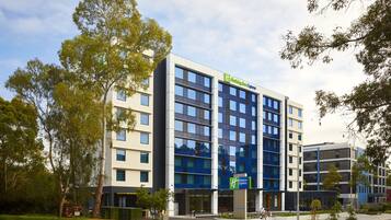 A modern hotel building with a prominent 'Holiday Inn Express' sign, multiple floors, and a parking lot in front.
