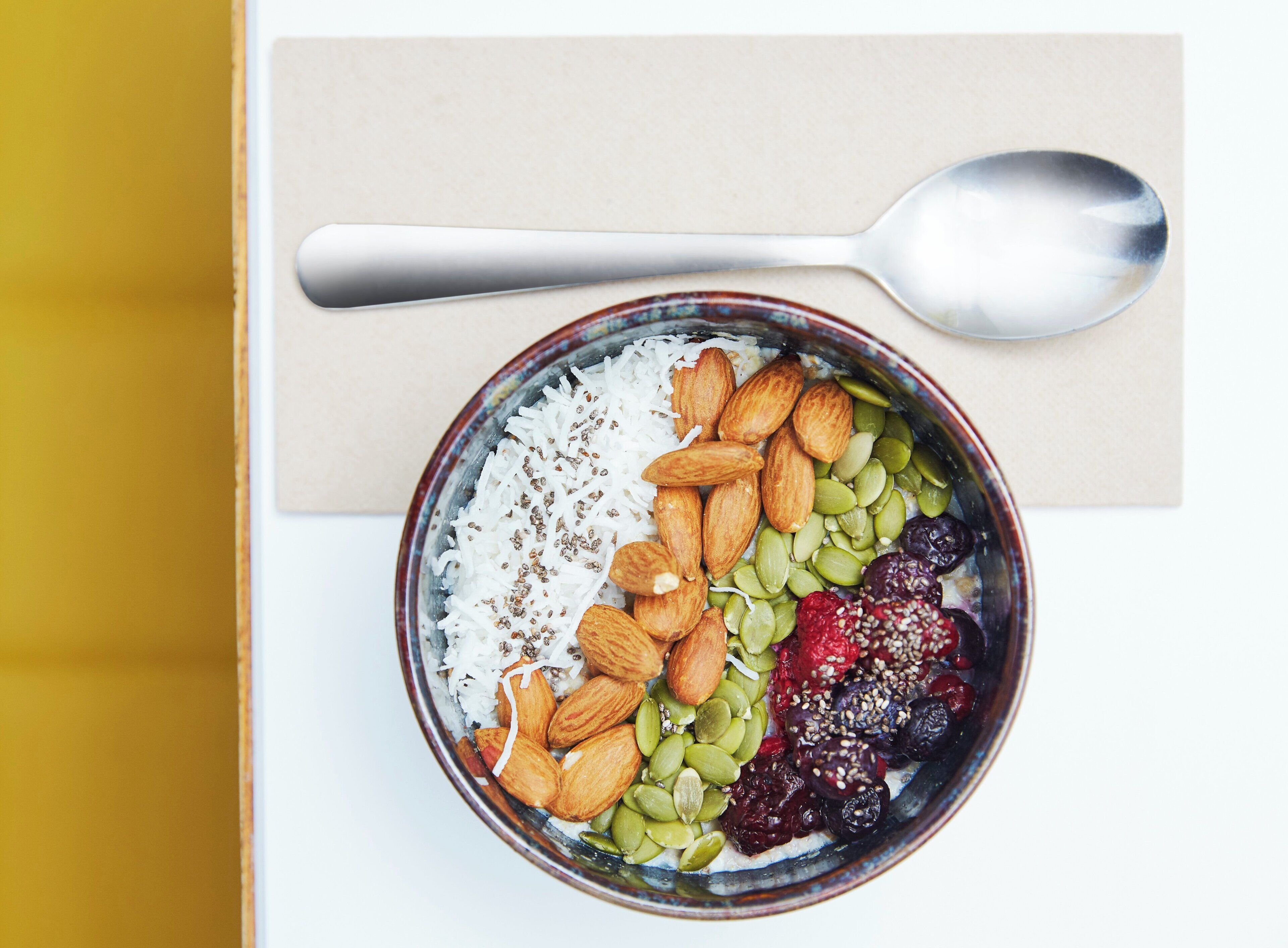 Un bol contenant des aliments, notamment du riz, des amandes, des graines de courge et des fruits secs, posé sur une surface blanche.
