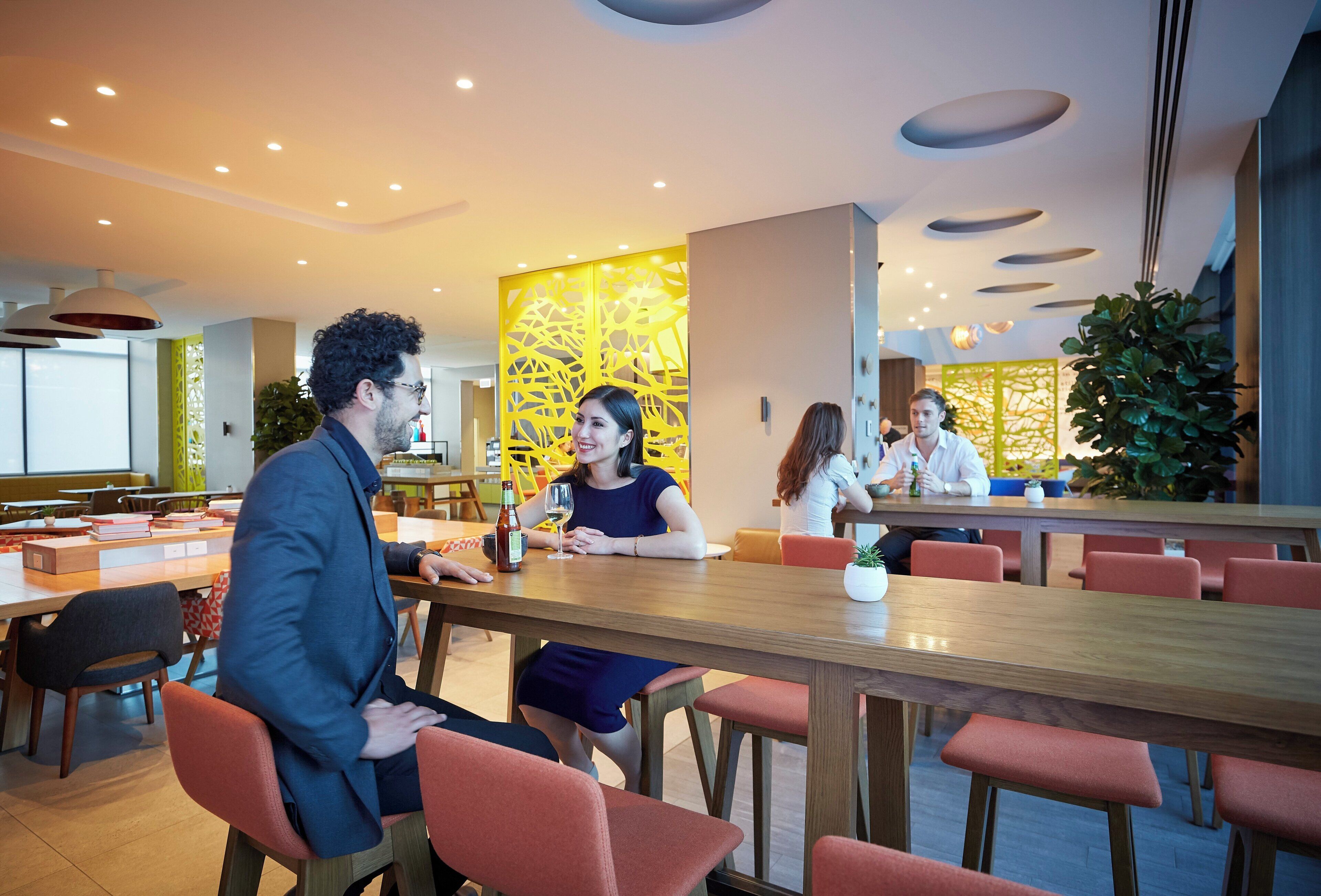 A modern dining area with wooden tables and red chairs, a yellow decorative wall, and recessed ceiling lighting.