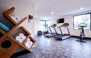 Une salle de sport moderne équipée de matériel d’exercice, d’un porte-serviettes en bois et de grandes fenêtres.