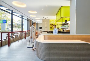 Un espace d’accueil d’hôtel au design moderne, comprenant un comptoir d’accueil incurvé, un coin salon avec des fauteuils et une vue sur l’extérieur grâce à de grandes fenêtres.