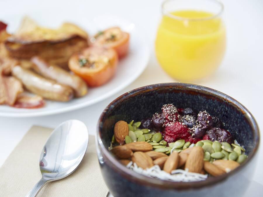 A breakfast setting with a bowl of mixed nuts and seeds, a plate of bacon and eggs, and a glass of orange juice.