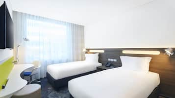 Una habitación de hotel con dos camas, un escritorio, una silla, un televisor y una lámpara.