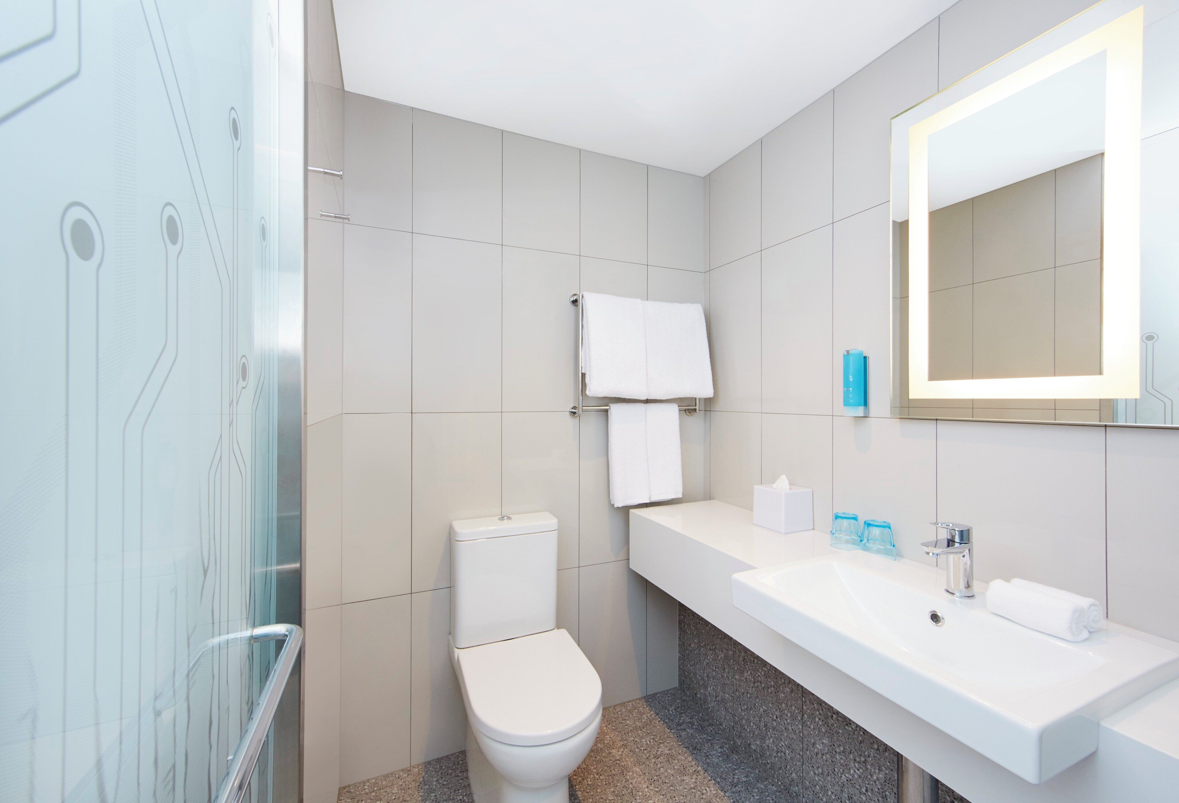 A modern bathroom with a toilet, sink, mirror, and glass shower enclosure.