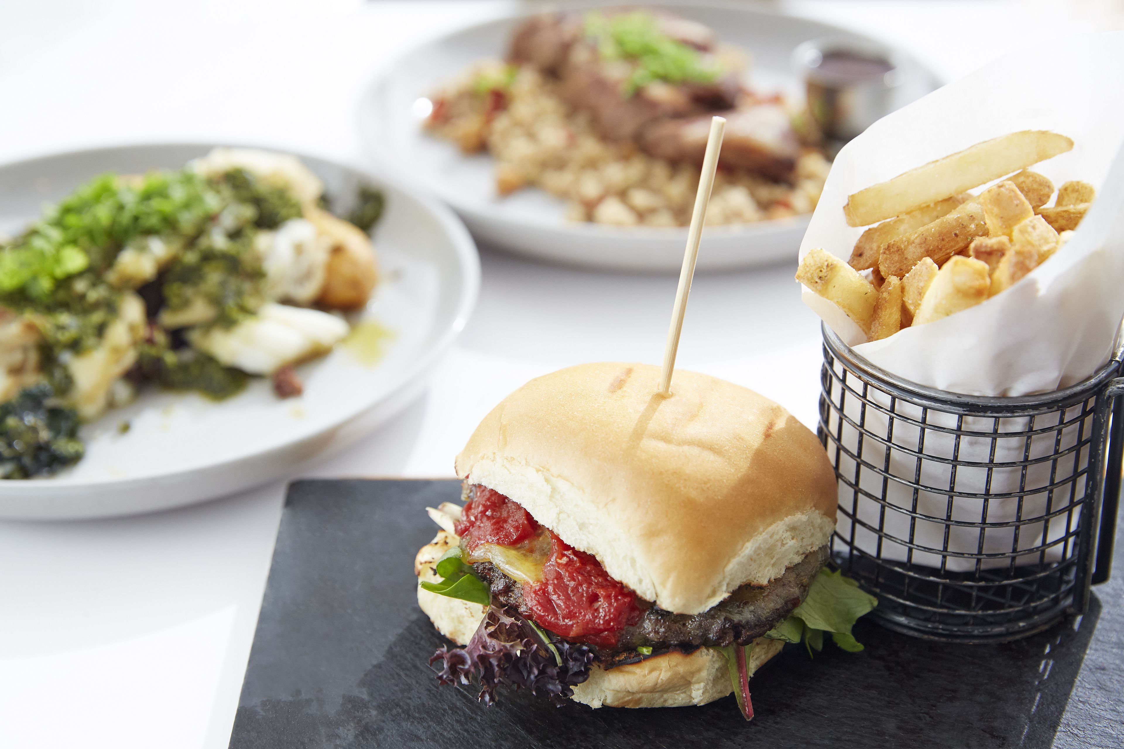 Een sandwich met een cocktailprikker, een mandje friet en een bord eten.