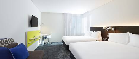 A hotel room with two beds, a desk with a chair, a TV, a phone, and a window with curtains.