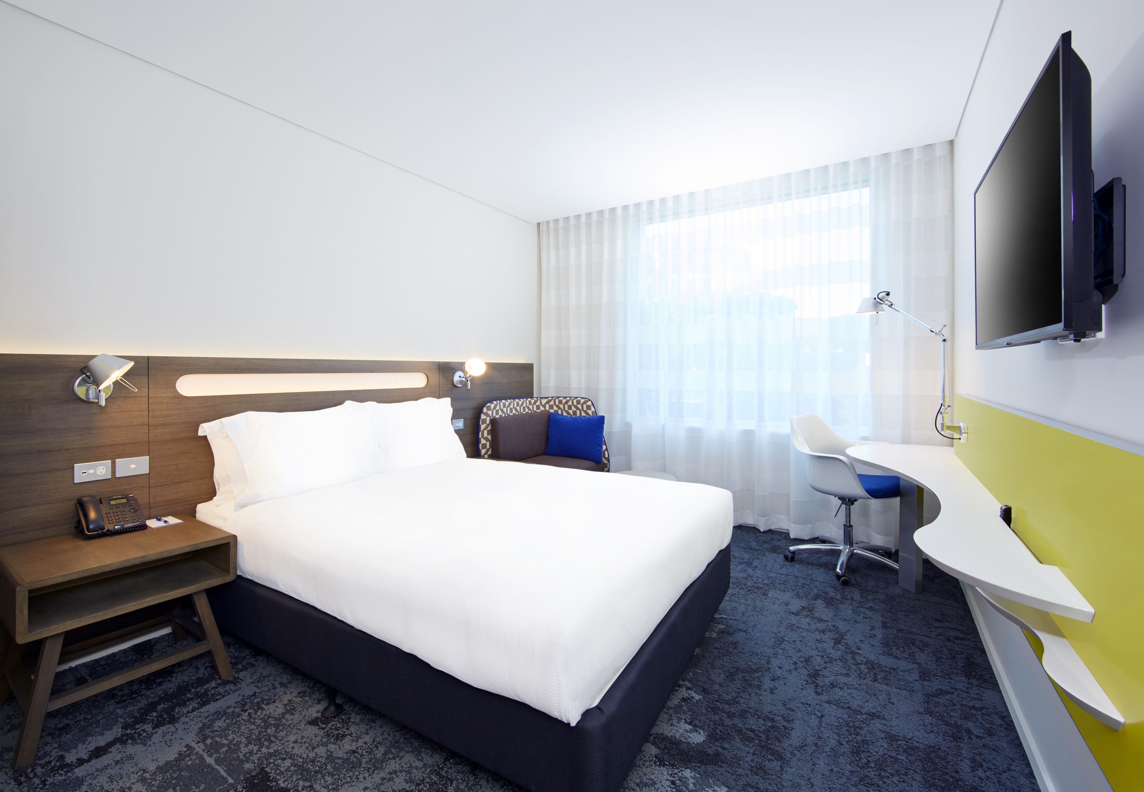 Une chambre d’hôtel avec un grand lit, un bureau, une chaise, une télévision et un téléphone sur la table de chevet.
