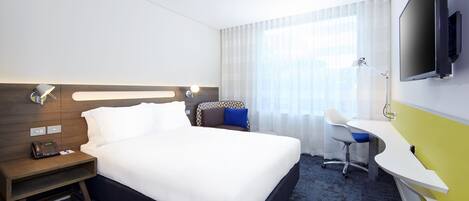Une chambre d’hôtel avec un grand lit, un bureau, une chaise, une télévision et un téléphone sur la table de chevet.