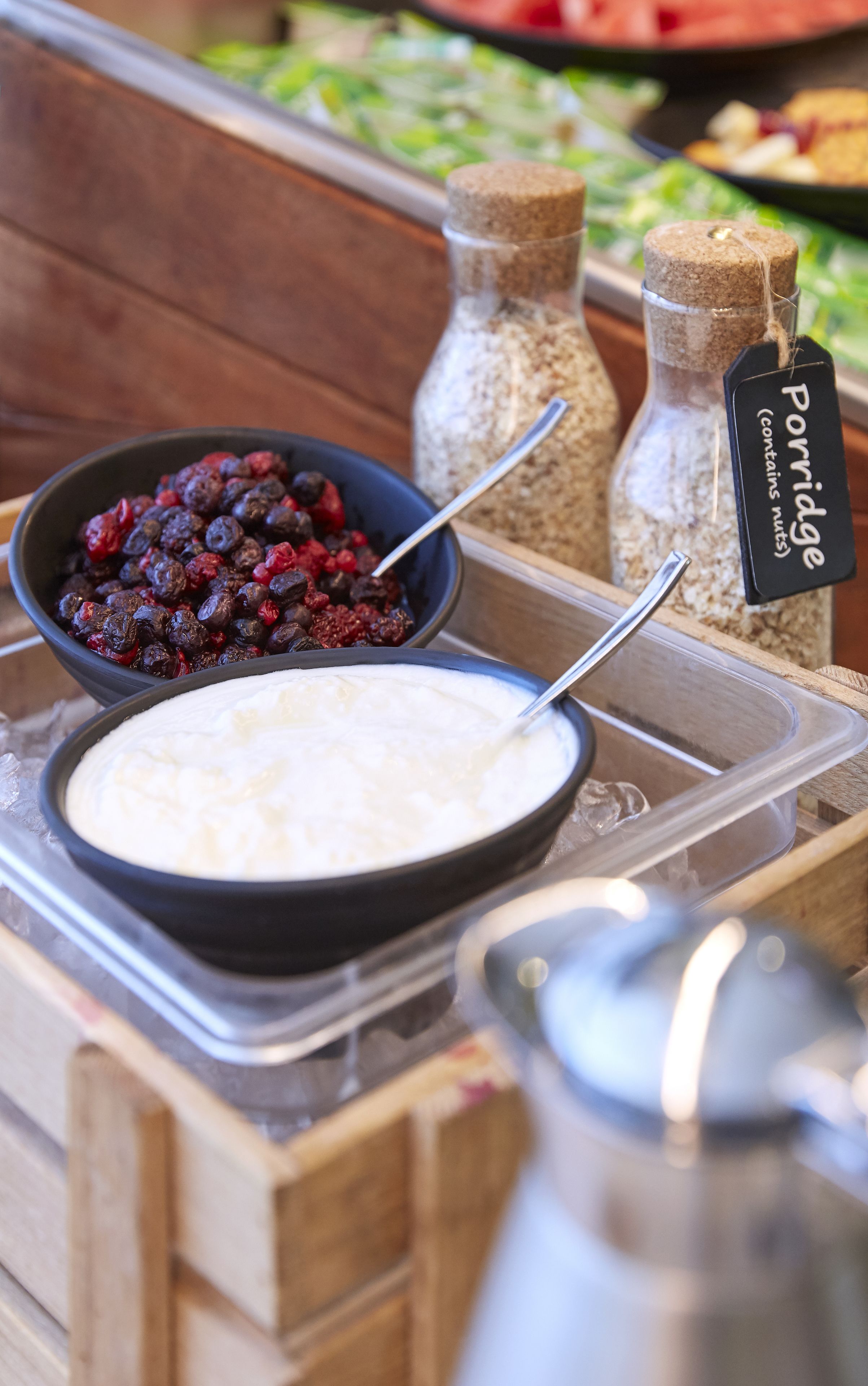 A buffet with bowls of porridge and berries, a jar labeled 'Poridge (contains nuts)', and a pitcher.
