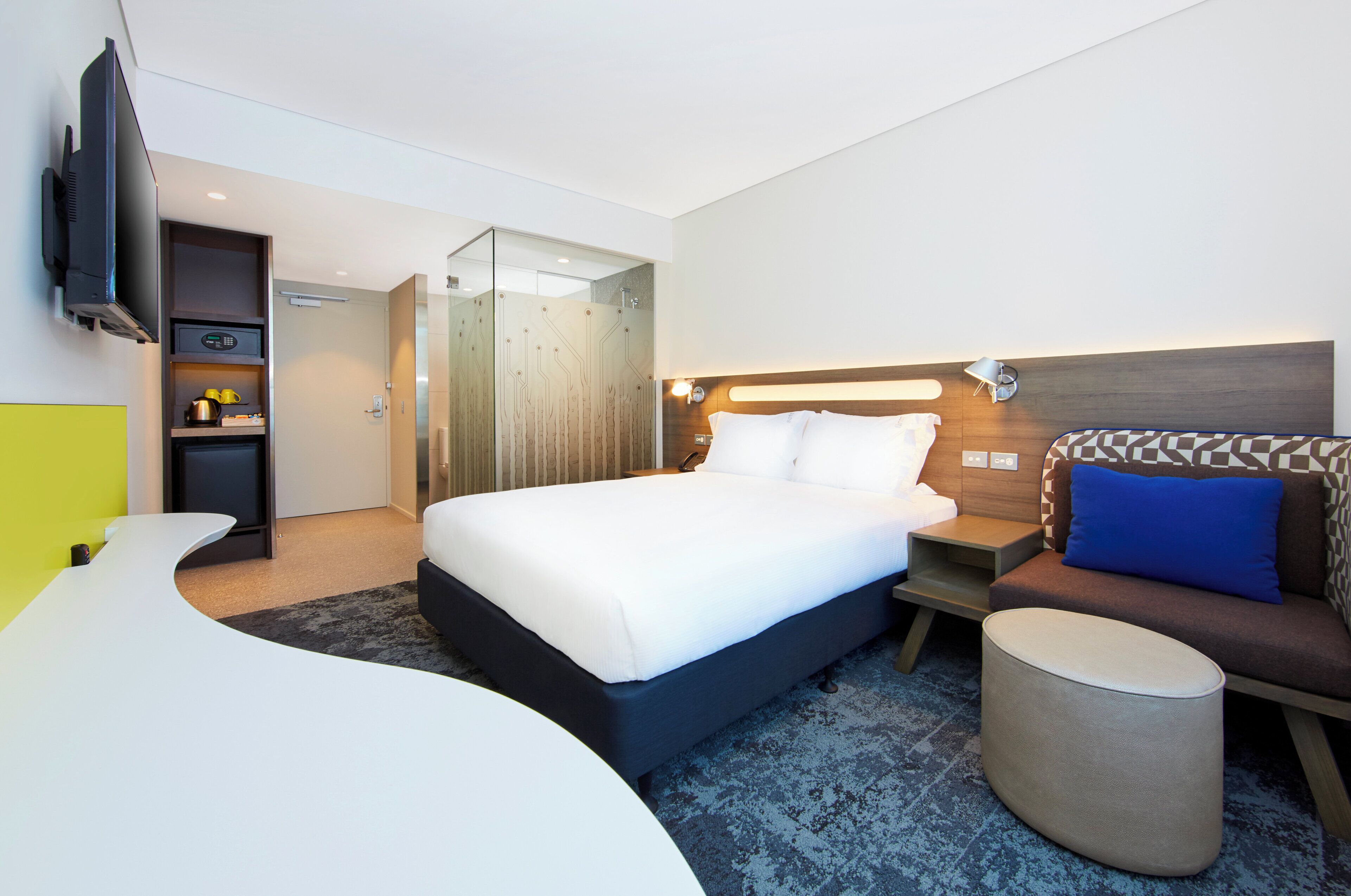 A modern hotel room with a bed, a sofa, a TV, a desk, and a bathroom.