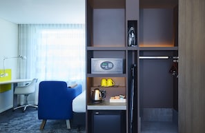 Una habitación de hotel compacta con kitchenette, un escritorio, una silla y un refrigerador pequeño.