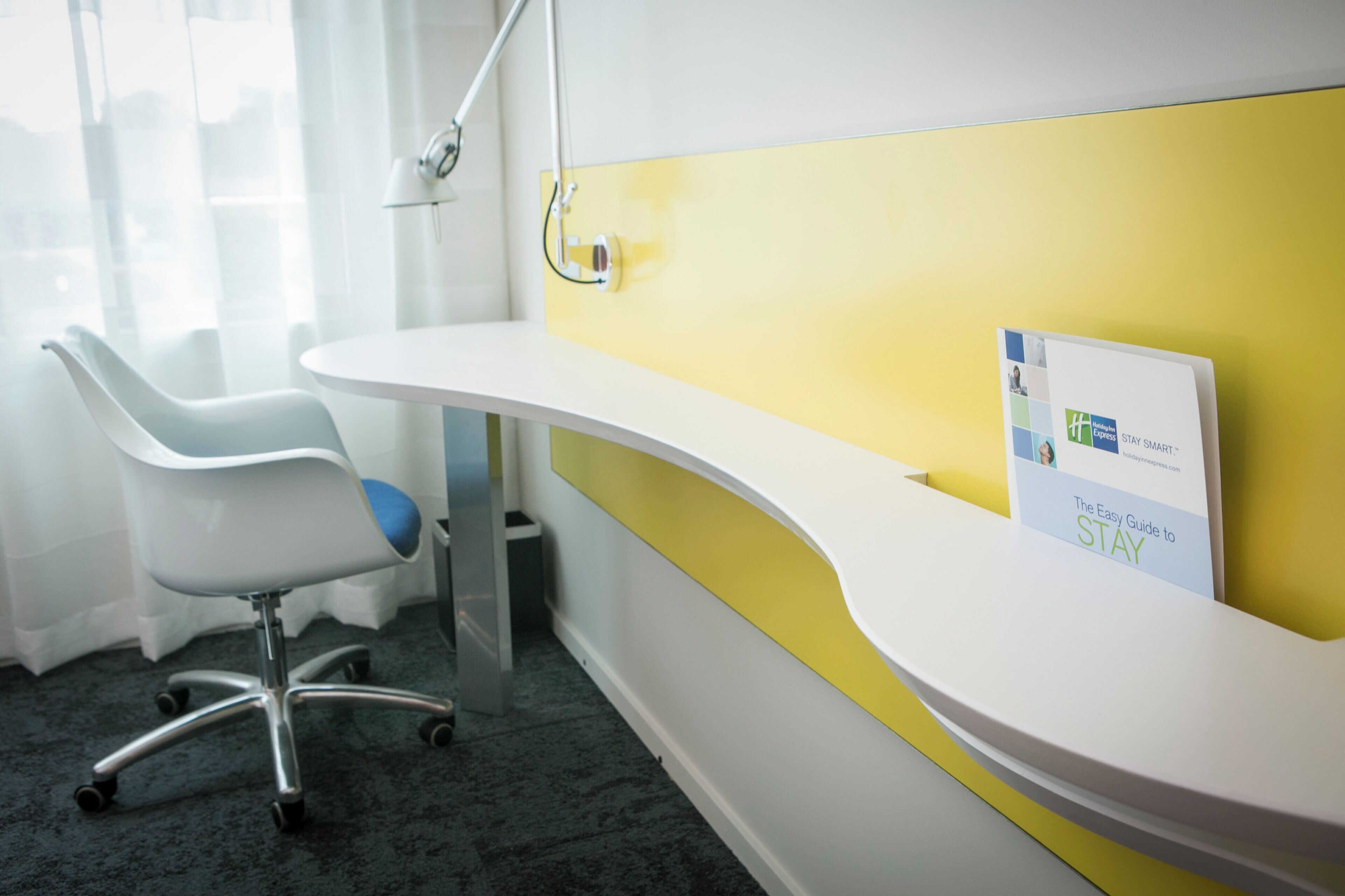 A reception desk with a yellow accent wall, a white chair, and a small trash bin.