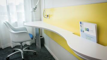 A reception desk with a yellow accent wall, a white chair, and a small trash bin.