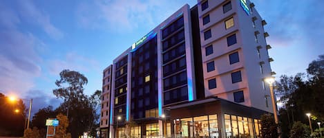 A multi-story Holiday Inn Express hotel with a modern design, featuring a prominent entrance and a landscaped outdoor area.
