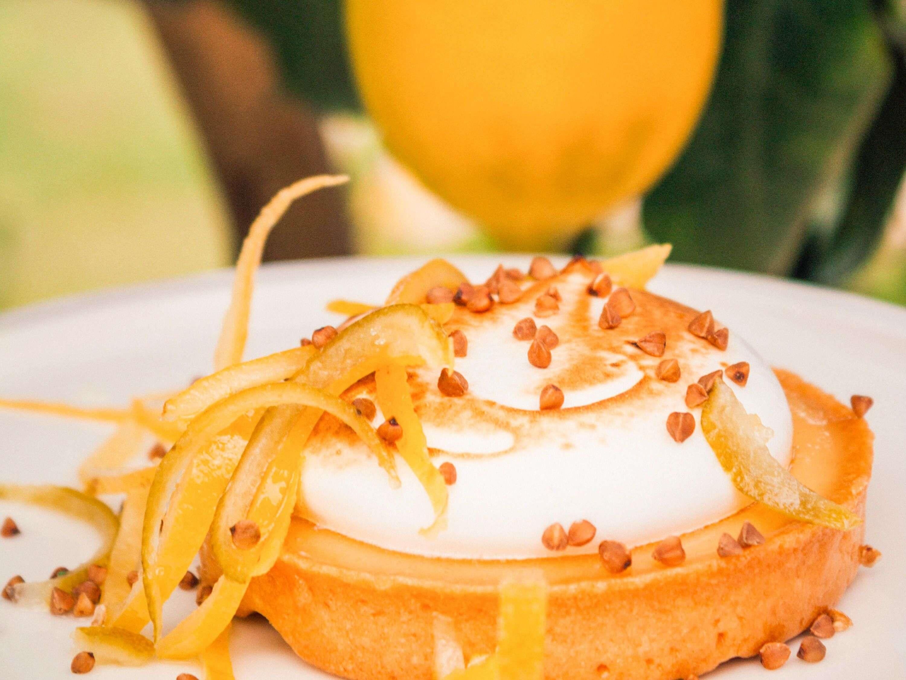 Un postre con cobertura cremosa, rodajas de fruta y nueces sobre un plato blanco.