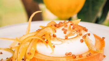 Un postre con cobertura cremosa, rodajas de fruta y nueces sobre un plato blanco.