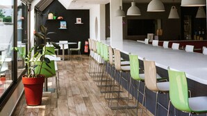 A modern indoor space with a long counter, green chairs, and a potted plant. - Ibis Styles Toulouse Labège (Labege)