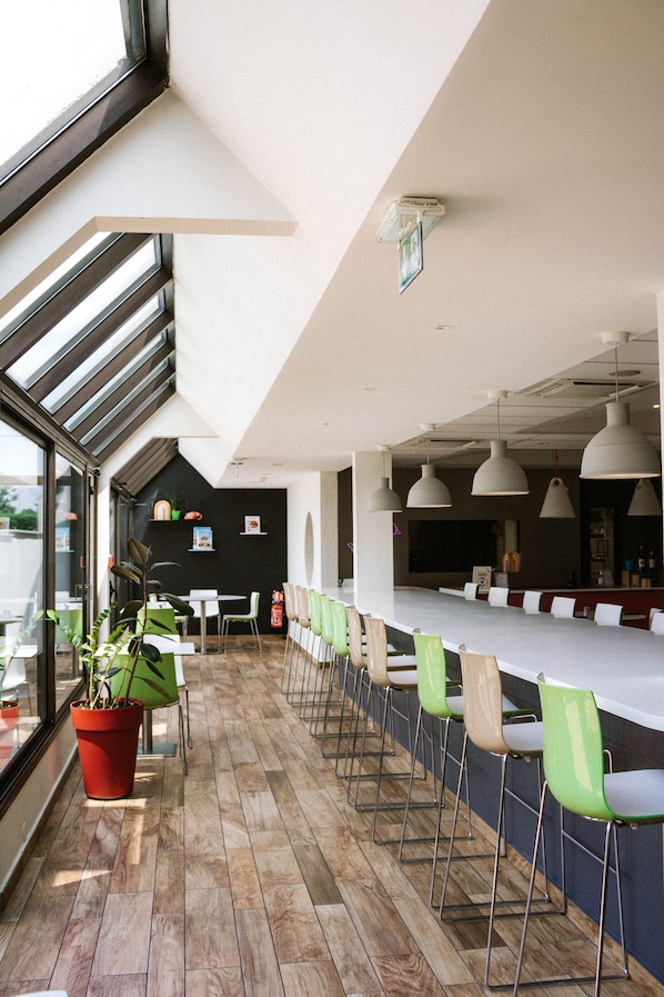 Un espacio interior moderno con una larga barra, sillas verdes y una planta en maceta.