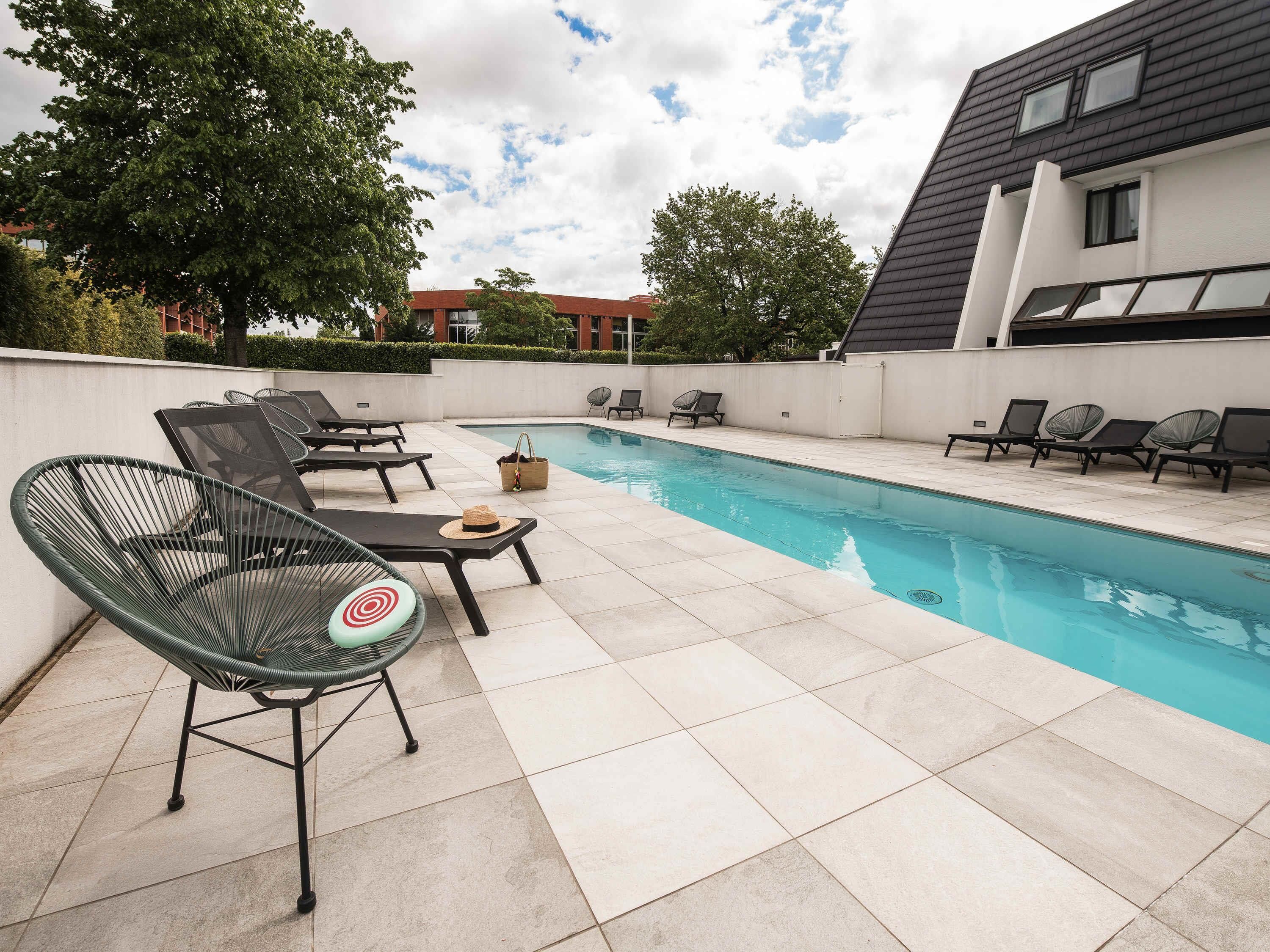 Une piscine avec des chaises longues et un bâtiment moderne en arrière-plan.