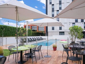 A poolside area with lounge chairs, umbrellas, and a dining table with chairs. - Ibis Styles Toulouse Labège (Labege)