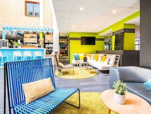 Un área de descanso moderna con asientos, un bar y una pared decorada en tonos verdes.