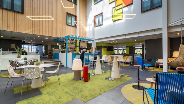 A modern indoor space with a bar area, seating arrangements, and a staircase. - Ibis Styles Toulouse Labège (Labege)