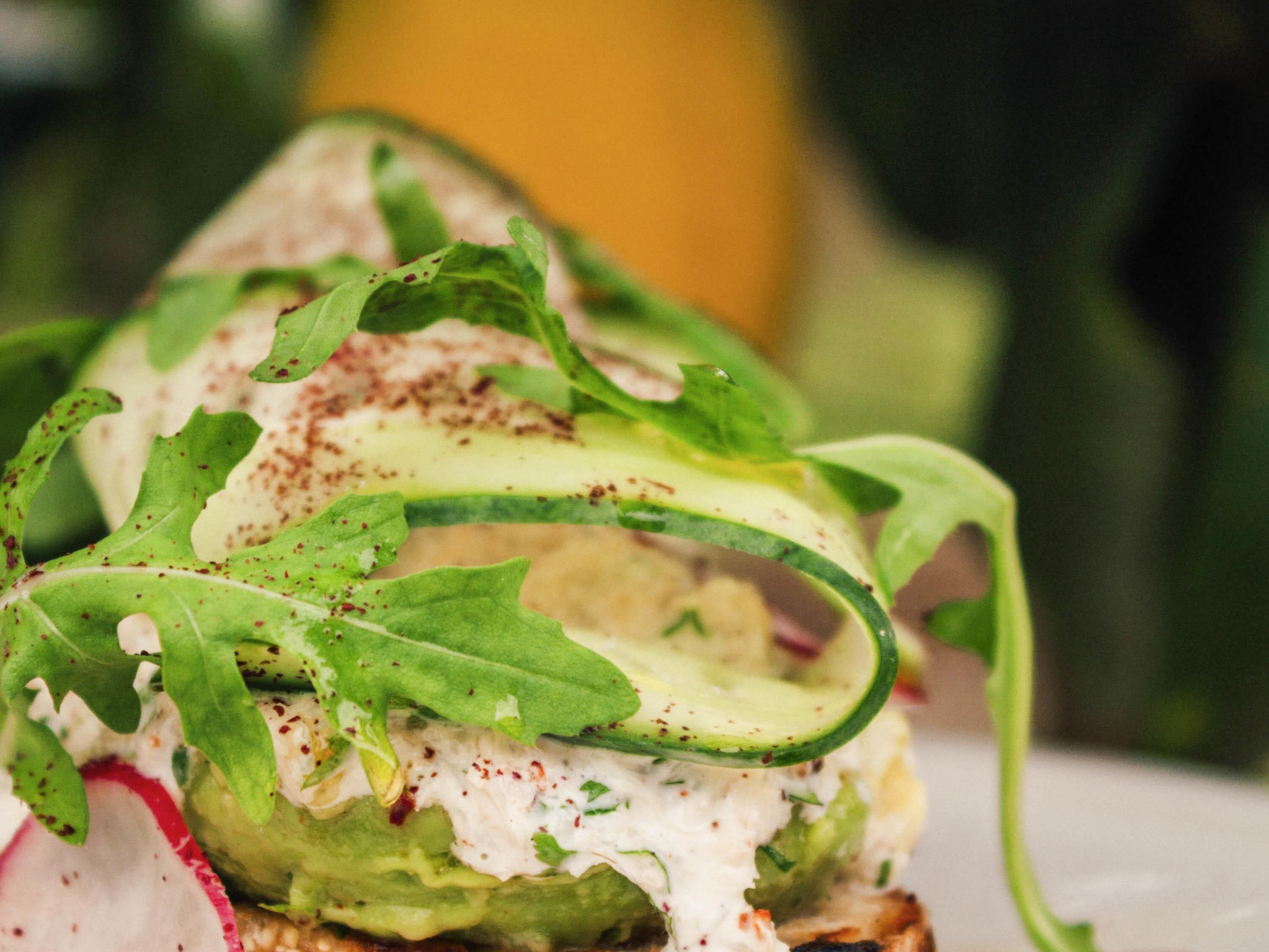 A close-up of a salad with arugula, radish, and cucumber, with a creamy dressing.