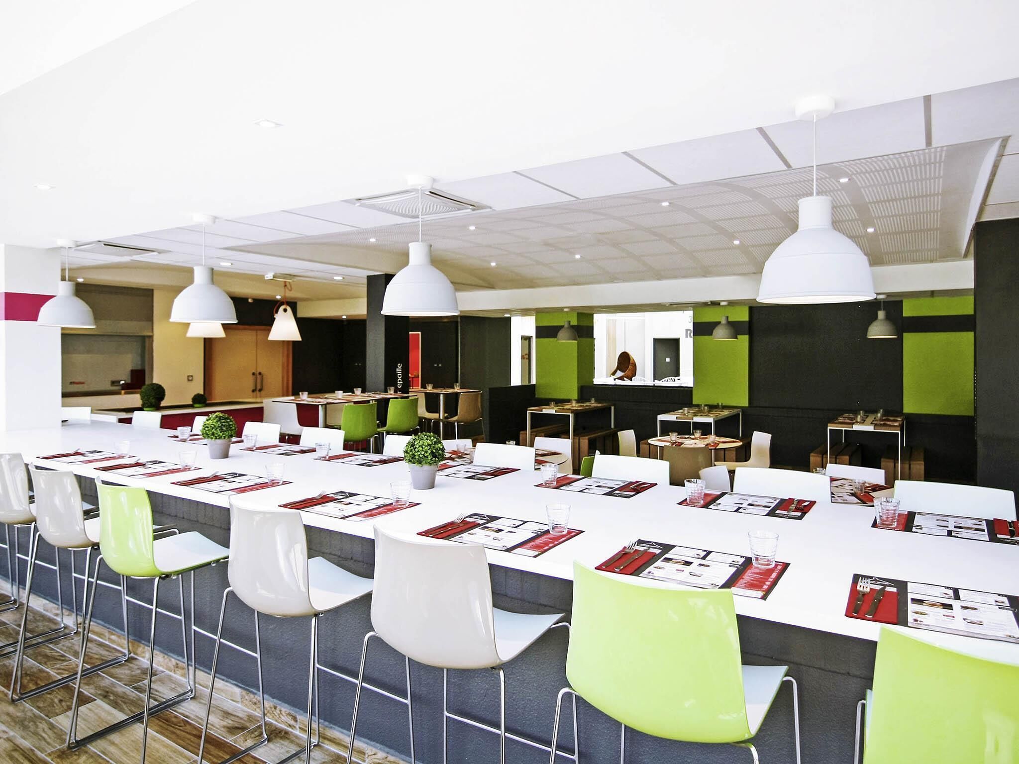 A modern dining area with white tables, green chairs, and pendant lighting.