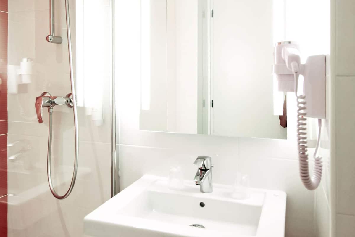 A bathroom with a white sink, a handheld showerhead, a mirror, and a hairdryer mounted on the wall.