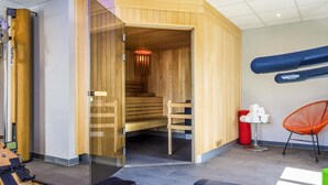 A modern spa room with a wooden sauna, a massage table, a red chair, and a treadmill. - Ibis Styles Toulouse Labège (Labege)